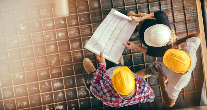 Tres ingenieros de una constructora sobre la losa de una obra revisando un plano