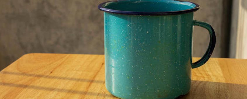 Pocillo de peltre de color azul colocado sobre un a mesa de madera - que es aleación