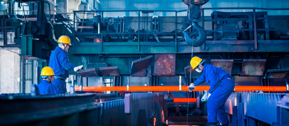 Trabajadores de la industria metalúrgica manipulando un perfil de acero al rojo vivo
