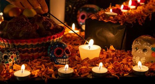 Acercamiento de un altar de día de muertos con calaveras, flores, pan y veladoras
