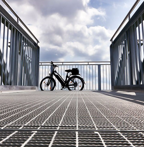 Piso de rejilla electroforjada dentada den un puente, al fondo de este esta recargada una bicicleta.